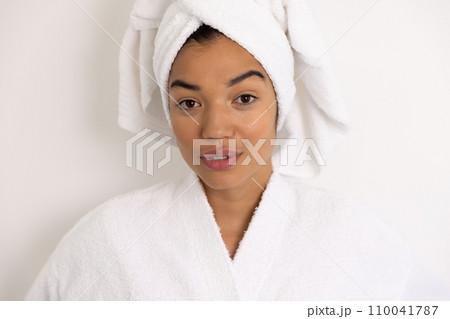 Portrait of happy biracial woman in bathrobe and with towel against white wall Portrait of happy biracial woman in bathrobe and with towel against white wall 110041787