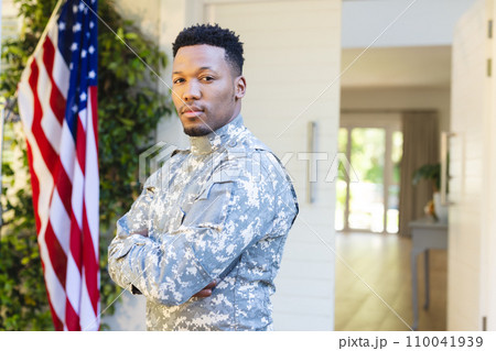 African american male soldier standing with arms crossed outside home and american flag, copy space 110041939