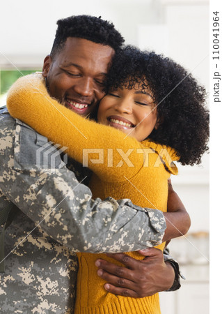 Happy african american male soldier embracing wife at home, copy space 110041964
