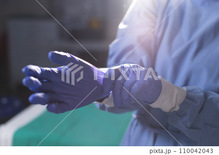 Midsection of biracial female surgeon wearing surgical gown and medical gloves in operating theatre Midsection of biracial female surgeon wearing surgical gown and medical gloves in operating theatre 110042043