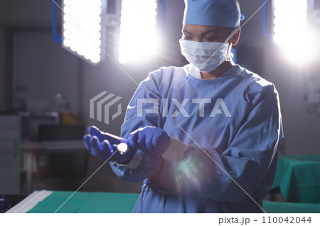 Biracial female surgeon wearing surgical gown and medical gloves in operating theatre Biracial female surgeon wearing surgical gown and medical gloves in operating theatre 110042044