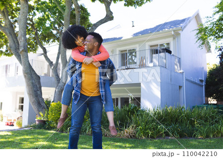 Happy african american couple riding piggyback in sunny garden, copy space 110042210