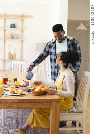 African american man pouring tea to cup at breakfast in morning at home, copy space 110042287