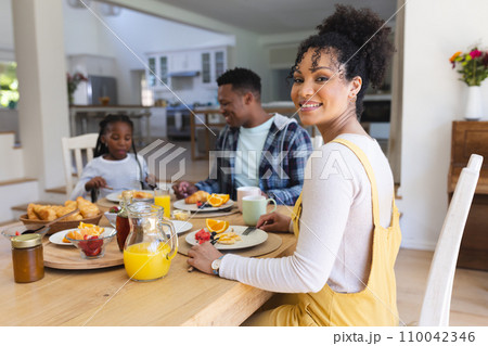 Happy african american woman sitting at table, having a snack with family at home, copy space 110042346