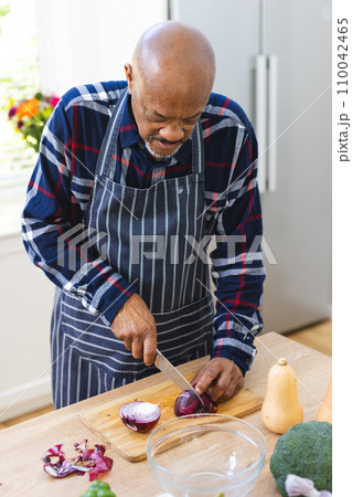 African american senior man in apron chopping onions in kitchen African american senior man in apron chopping onions in kitchen 110042465