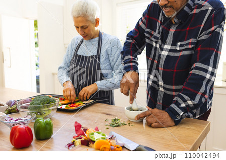 Diverse senior couple preparing healthy meal with vegetables in kitchen Diverse senior couple preparing healthy meal with vegetables in kitchen 110042494