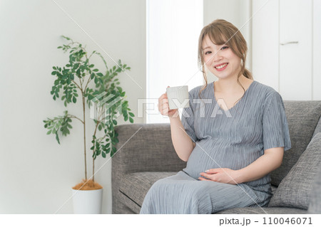 家のソファでホットドリンクを飲む妊婦の女性・マタニティ・プレママ 家のソファでホットドリンクを飲む妊婦の女性・マタニティ・プレママ 110046071