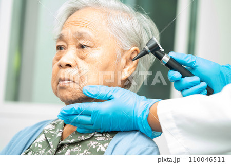 Audiologist or ENT doctor use otoscope checking ear of asian senior woman patient treating hearing loss problem. 110046511
