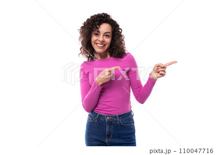 stylish slim young curly brunette woman dressed in a lilac turtleneck points her finger at the empty 110047716