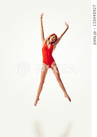 Beautiful young blonde woman in stylish red vintage swimsuit cheerfully jumping against white background Beautiful young blonde woman in stylish red vintage swimsuit cheerfully jumping against white background 110048927