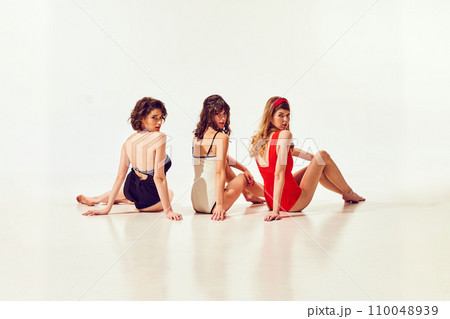 Elegant, beautiful young girls in stylish vintage swimsuit sitting and looking back against white background. Retro sport, cruise Elegant, beautiful young girls in stylish vintage swimsuit sitting and looking back against white background. Retro sport, cruise 110048939