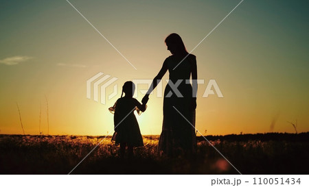 Mamma and daughter enjoying sunset in nature while walking in sun-drenched field 110051434