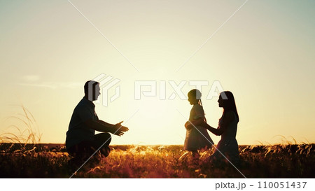 Family plays with daughter running to hugs of parents as sun sets behind rolling field 110051437