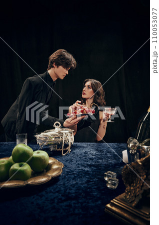 Handsome young man, waiter serving to elegant, beautiful woman plate with grapes. Luxurious dinner. Royal event Handsome young man, waiter serving to elegant, beautiful woman plate with grapes. Luxurious dinner. Royal event 110053077