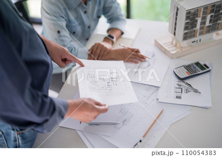 Male engineer architect explaining sketching about interior architectural building on blueprint to discussion and analysis technical for construction plan with partner together in workplace site 110054383