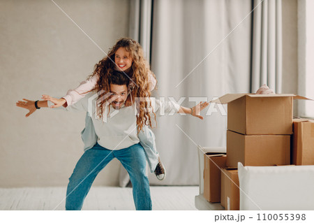 Happy young family couple man and woman playing and enjoys after moving cardboard boxes to new estate home apartment. Happy young family couple man and woman playing and enjoys after moving cardboard boxes to new estate home apartment. 110055398