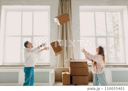 Happy young family couple man and woman throws cardboard boxes on new home. Moving delivery concept. Happy young family couple man and woman throws cardboard boxes on new home. Moving delivery concept. 110055401