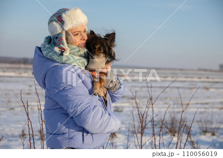 The woman has to keep her dog warm by putting the animal under her jacket. The woman has to keep her dog warm by putting the animal under her jacket. 110056019