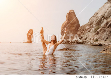 Woman sea fitness. Happy woman in a white bikini performing pilates in the sea on the beach. Female fitness yoga routine concept. Healthy lifestyle. 110056487