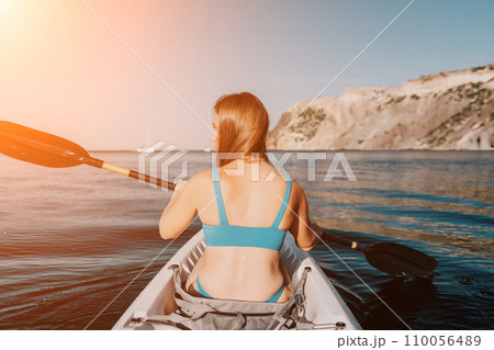 Woman in kayak back view. Happy young woman with long hair floating in kayak on calm sea. Summer holiday vacation and cheerful female people relaxing having fun on the boat. 110056489