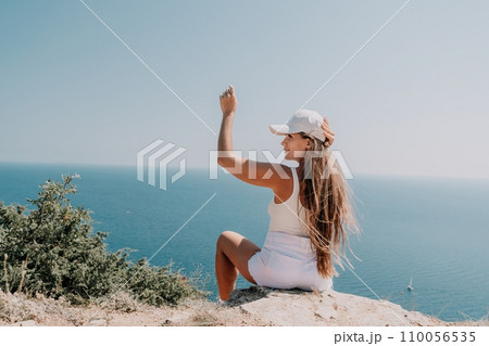 Woman summer travel sea. Happy tourist enjoy taking picture outdoors for memories. Woman traveler posing over sea bay surrounded by volcanic mountains, sharing travel adventure journey 110056535