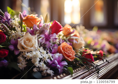 A lovely dark wood coffin adorned with roses, lilies, and carnations creates a lush display. Shot up close, the image captures intricate details, enhanced by soft, diffused light for a warm atmosphere A lovely dark wood coffin adorned with roses, lilies, and carnations creates a lush display. Shot up close, the image captures intricate details, enhanced by soft, diffused light for a warm atmosphere 110056799