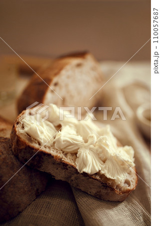 Close up photo of pieces of delicious, hot homemade loaf of bread with fresh homemade butter lying in natural fabric on wooden table. 110057687