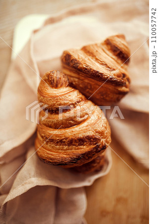 Top view photo of golden brown color, with typical crescent shape and flaky, buttery crust croissants sitting in natural fabric on wooden table Top view photo of golden brown color, with typical crescent shape and flaky, buttery crust croissants sitting in natural fabric on wooden table 110057742