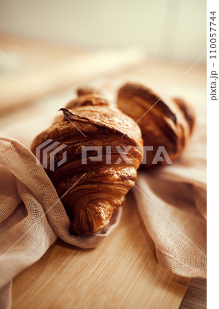 Two golden brown color, with typical crescent shape and flaky, buttery crust croissants sitting in natural cotton fabric on wooden table 110057744