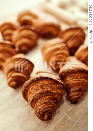 Close up photo of group of croissants with golden brown color and have flaky, buttery crust, sitting on top of white paper bag on table. 110057750