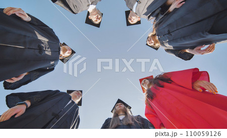Graduates in robes stand in a circle. View from below. Graduates in robes stand in a circle. View from below. 110059126