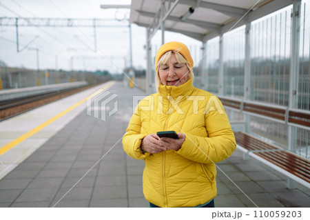 Portrait of 50s senior woman using mobile phone while waiting on tram station.  110059203