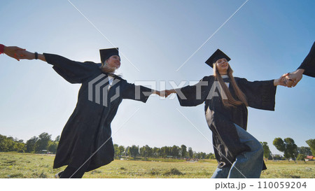 College graduates holding hands run in a round dance. 110059204