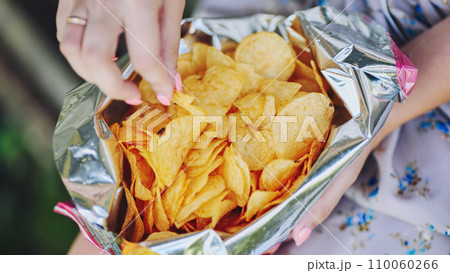 A girl eating chips on a summer afternoon. A pack of chips in close-up. 110060266