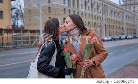 Two young women kissing each other on a city 110060275