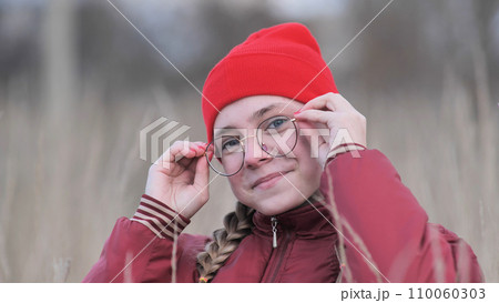 Portrait of a teenage girl in glasses standing in tall grass in the fall. Portrait of a teenage girl in glasses standing in tall grass in the fall. 110060303