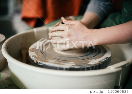 Close-up of a woman hands moulding a ceramic piece on the potter's wheel Creating a ceramic mould from clay in potters workshop Close-up of a woman hands moulding a ceramic piece on the potter's wheel Creating a ceramic mould from clay in potters workshop 110060682