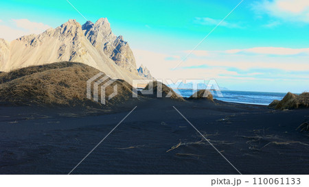 Icelandic stokksnes black sand beach with vestrahorn mountains creating spectacular scandinavian natural landscape. Beautiful ocean coastline with massive hills in iceland. Handheld shot. Icelandic stokksnes black sand beach with vestrahorn mountains creating spectacular scandinavian natural landscape. Beautiful ocean coastline with massive hills in iceland. Handheld shot. 110061133