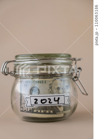 Saving Money In Glass Jar filled with Dollars banknotes. 2024 year transcription in front of jar. Managing personal finances extra income for future insecurity Saving Money In Glass Jar filled with Dollars banknotes. 2024 year transcription in front of jar. Managing personal finances extra income for future insecurity 110063186
