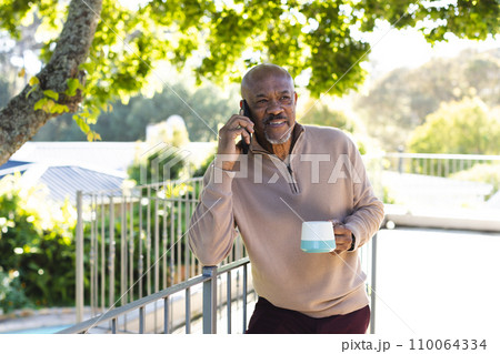 African american senior man holding cup of coffee and talking on smartphone on sunny terrace African american senior man holding cup of coffee and talking on smartphone on sunny terrace 110064334