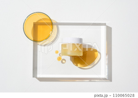 Close-up of a jar of unbranded cosmetics displayed on a transparent glass platform with drops of honey. Honey is used as a very good skin moisturizer. Close-up of a jar of unbranded cosmetics displayed on a transparent glass platform with drops of honey. Honey is used as a very good skin moisturizer. 110065028