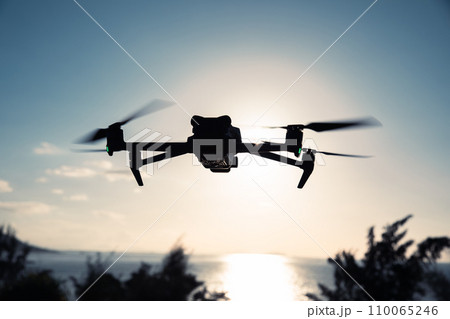Silhouette of flying drone which taking photo over sunrise sea 110065246