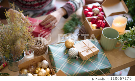 Young asian woman in sweater wrapping christmas gift and decorating with hemp rope while preparing toys ornaments and presents to celebrate for christmas festive holiday and winter seasons at house 110067179