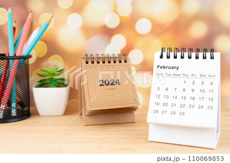 White February 2024 desk calendar on wooden table with gold light bokeh background. 110069853