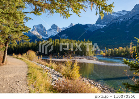 Beautiful Bow River scenery. Canmore, Alberta, Canada. The Three Sisters trio of peaks over the blue sky in the background. Beautiful Bow River scenery. Canmore, Alberta, Canada. The Three Sisters trio of peaks over the blue sky in the background. 110070550