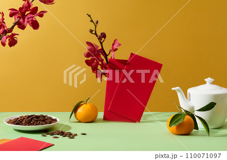Fresh orchid branches decorate the background. A plate of melon seeds, a pot of tea, tangerines and lucky money envelopes are displayed on the table. Front view. 110071097