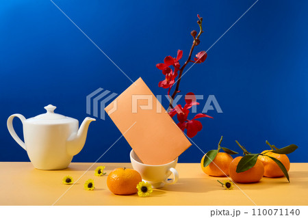 Displayed on a table against a blue background, a front view showcases a tea set, tangerines, and fresh flowers-providing space for Tet themed advertising. 110071140