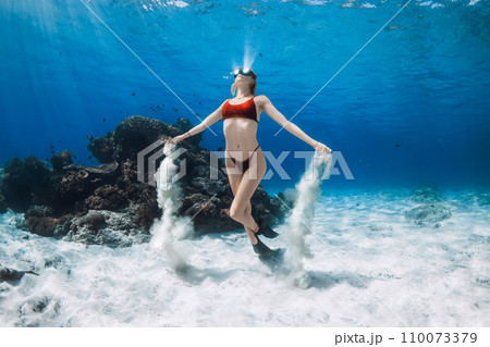 Free diver swims underwater and playing with sand. Freediving with attractive woman in clear blue sea 110073379