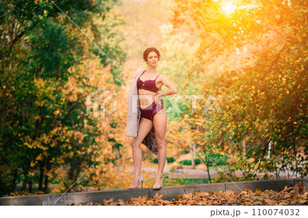 Young beautiful dark-haired woman with slender figure in lingerie and classic coat in autumn park Young beautiful dark-haired woman with slender figure in lingerie and classic coat in autumn park 110074032
