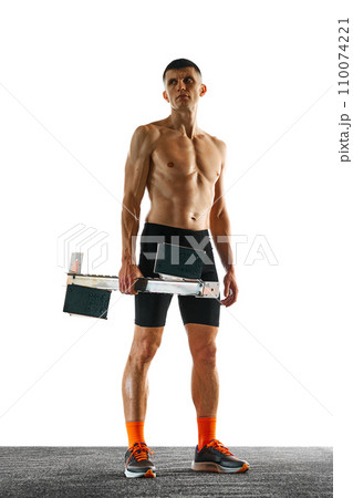 Full length portrait of young athletic man, with muscular build body stands holding starting blocks before championship against white background. 110074221